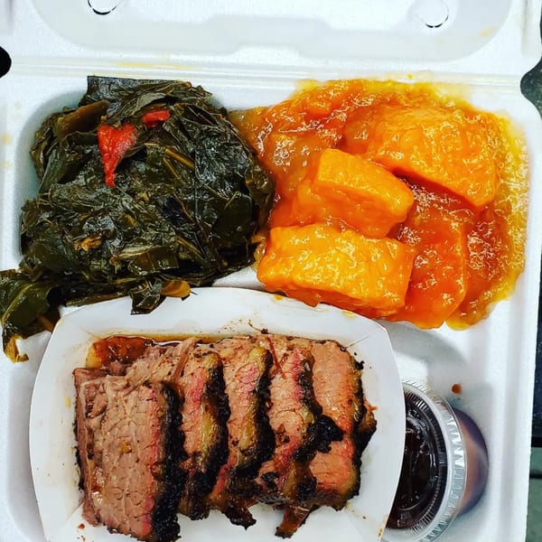 Village BBQ brisket meal with collard greens, candied yams, and a side of barbecue sauce.