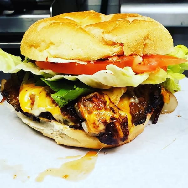 A Village BBQ burger with melted cheese, caramelized onions, lettuce, and tomato on a bun.