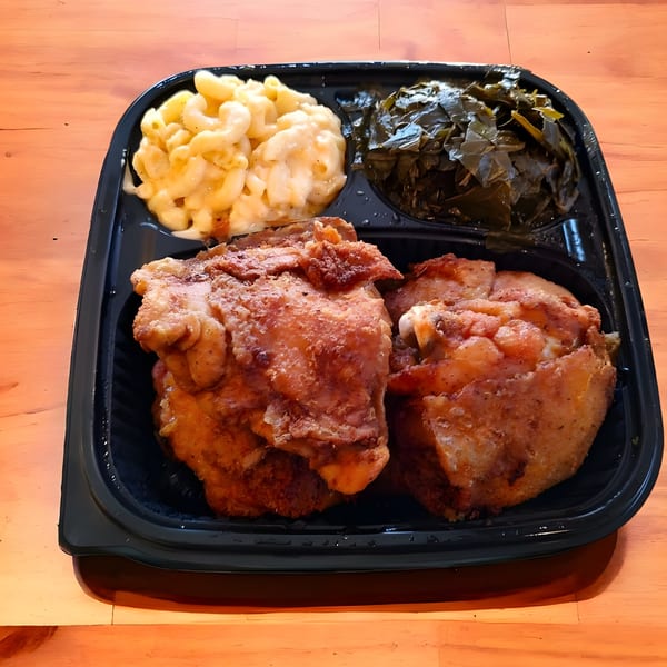 Village BBQ fried chicken with macaroni and cheese and collard greens in a black to-go container.