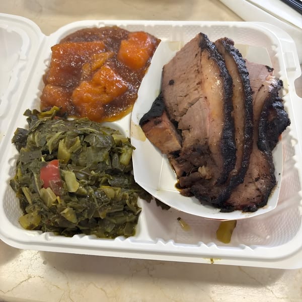 Village BBQ brisket with collard greens and candied yams in a white takeout container.