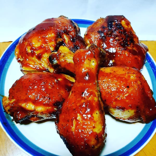 Five pieces of Village BBQ chicken, glazed with a rich, red barbecue sauce, on a white plate.